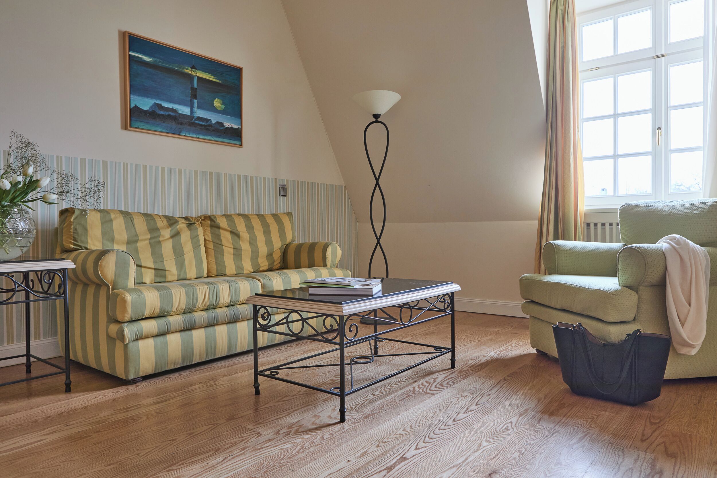 A living room with a striped sofa, a coffee table, a lamp, a chair, and a window with curtains.