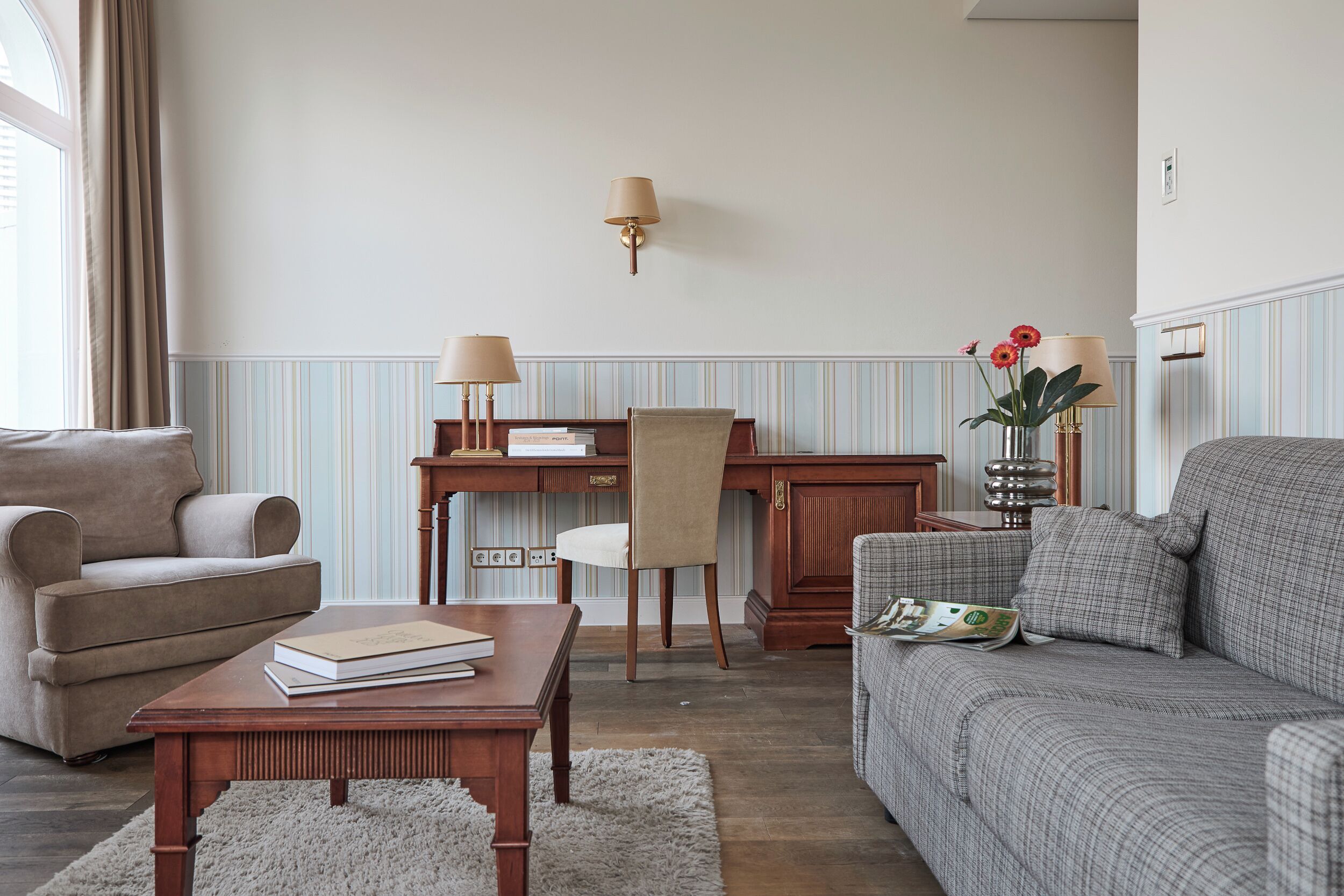 Ein Wohnzimmer mit Sofa, Sessel, Couchtisch aus Holz und Schreibtisch mit Stuhl.
