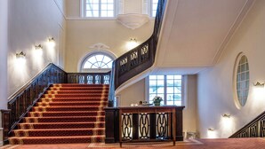 A grand staircase with ornate railings, a polished wooden finish, and a carpeted landing area. - ATLANTIC Grand Hotel Travemünde (Lübeck)