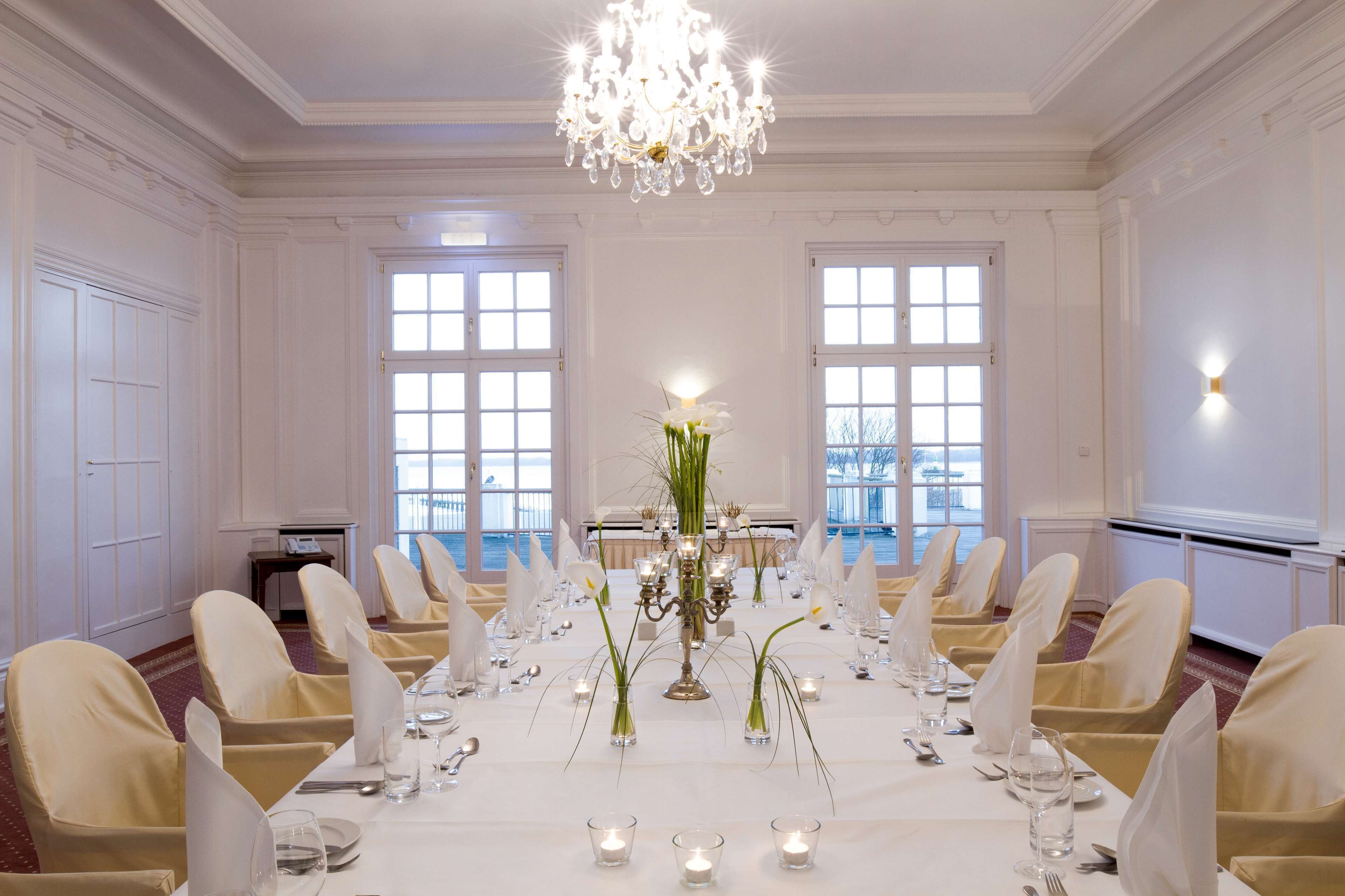 Een stijlvolle eetzaal met een lange tafel gedekt voor een maaltijd, kroonluchters en grote ramen.