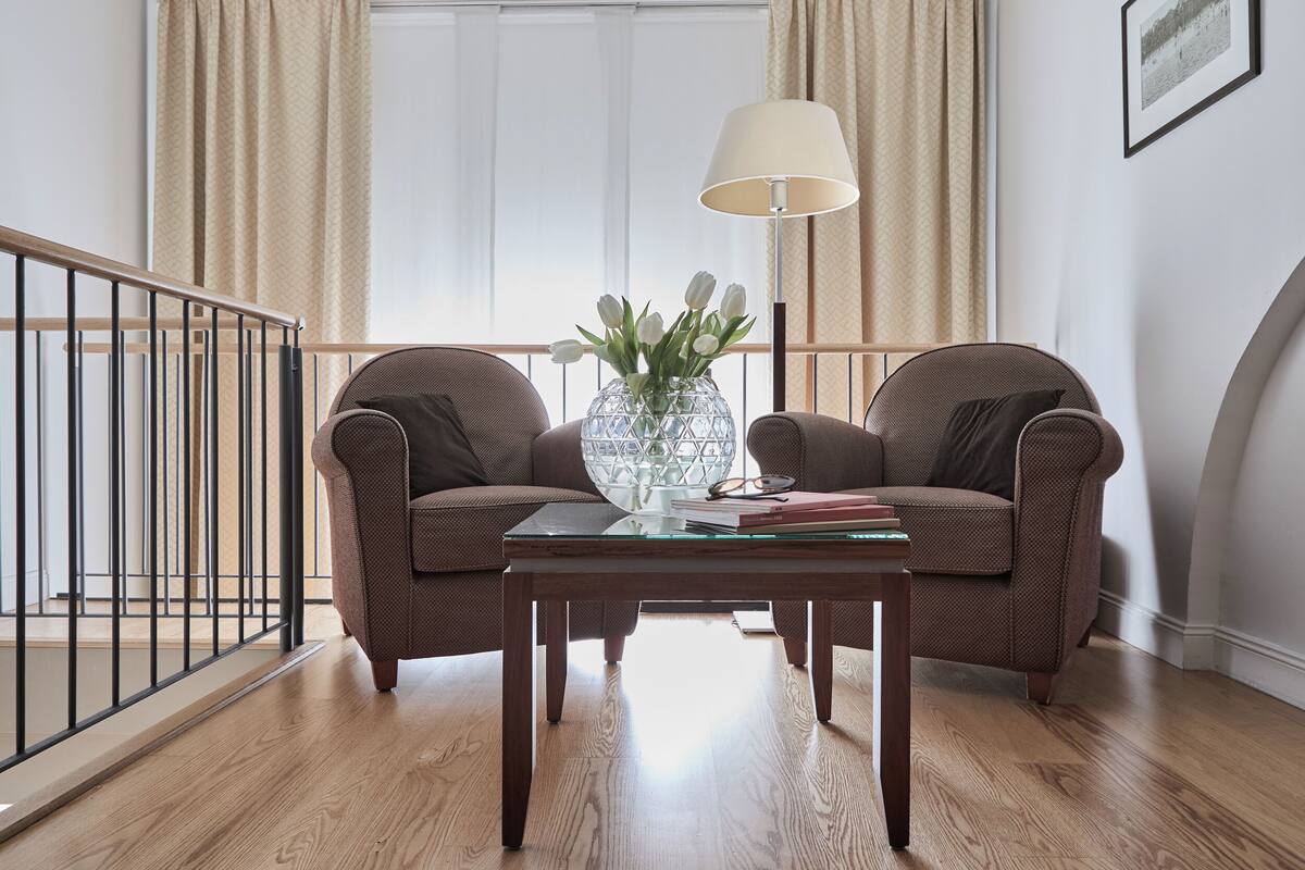 Una habitación con dos sillones marrones, una mesa de centro de vidrio, un jarrón con flores, una lámpara y un cuadro en la pared.