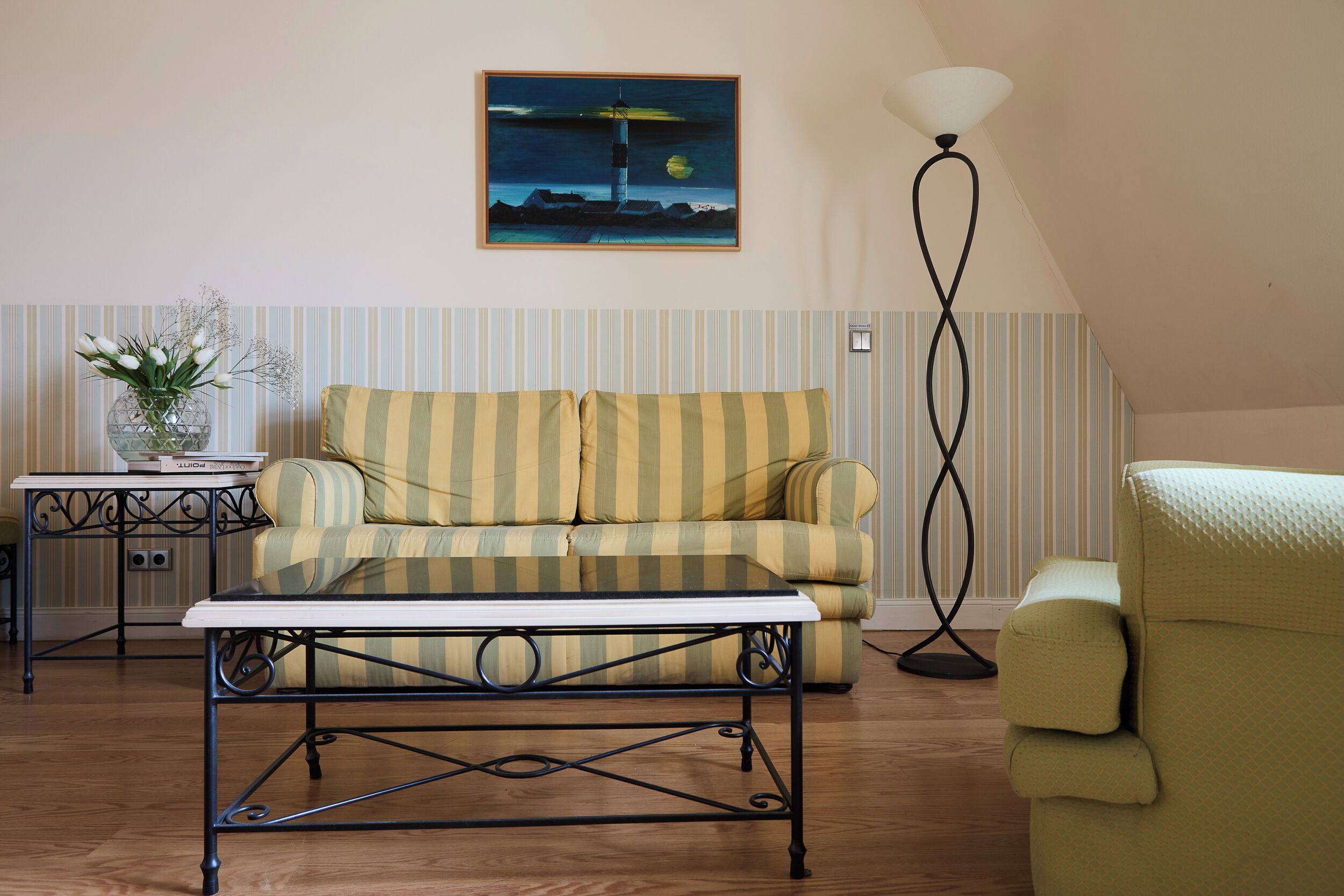 A living room with a striped sofa, a coffee table, a floor lamp, and a painting on the wall.