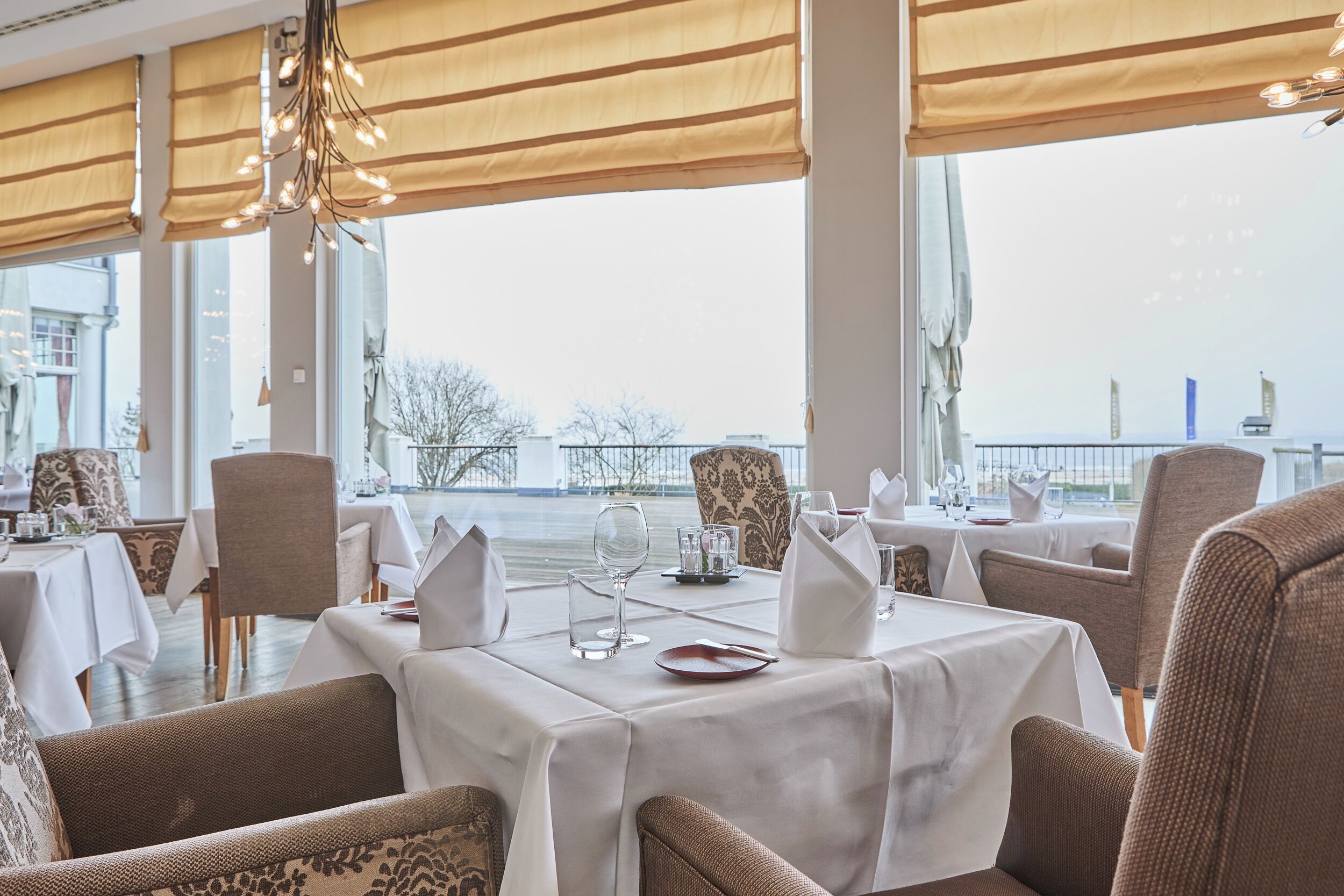 A restaurant with tables set for dining, large windows, and a view of a body of water.