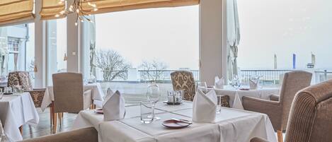A restaurant with tables set for dining, large windows, and a view of a body of water.