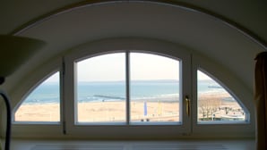 A room with a large arched window overlooking a beach and ocean. - ATLANTIC Grand Hotel Travemünde (Lübeck)