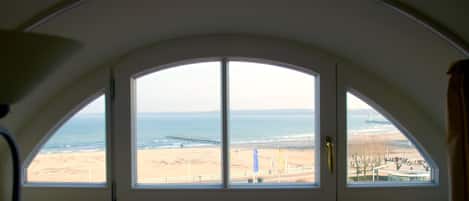 A room with a large arched window overlooking a beach and ocean.
