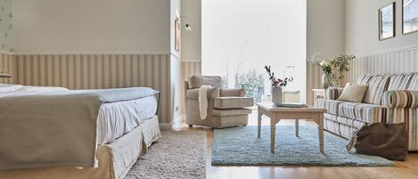 A bedroom with a bed, a chair, a sofa, a coffee table, and a view of the outdoors.