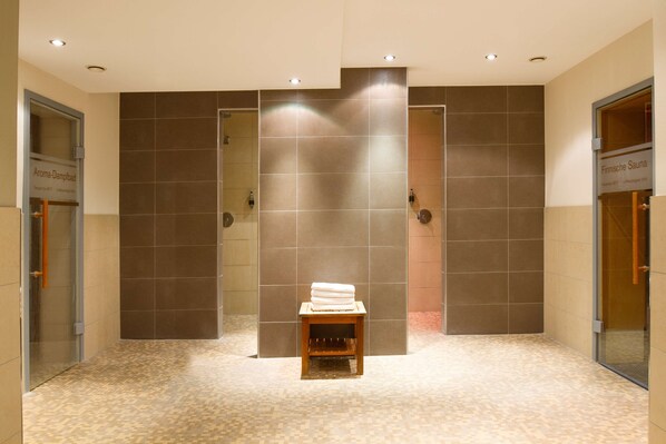 Un baño moderno con piso de baldosas, un banco de madera con toallas y puertas de vidrio que dicen "Aroma-Dampfbad" y "Finnische Sauna".