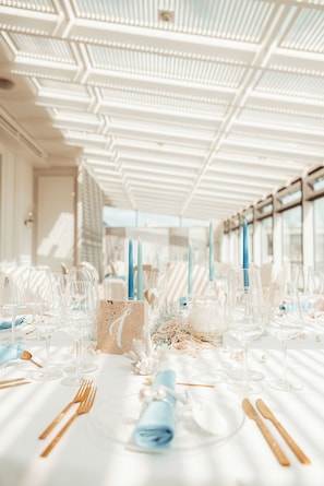Ein Festsaal mit gedeckten Tischen für eine festliche Veranstaltung, mit weißen Tischdecken, klarem Glas und blauen Akzenten.