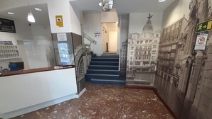 A lobby with a marble floor, a reception desk, a staircase, and a mural of a building. - Photo Zabalburu Hotel (Bilbao)