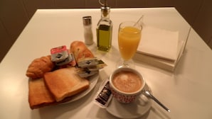 A breakfast setting with croissants, a sandwich, a cup of coffee, a glass of orange juice, and a bottle of olive oil on a white table. - Photo Zabalburu Hotel (Bilbao)