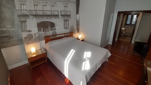A bedroom with a large bed, wooden headboard, bedside lamps, and a wall mural of a building. - Photo Zabalburu Hotel (Bilbao)