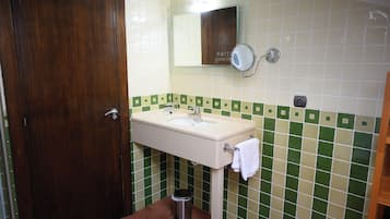 A bathroom with a wooden door, a sink with a mirror, and green and white tiled walls.