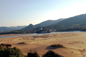 Un paisaje costero con una playa arenosa, un río y montañas al fondo.