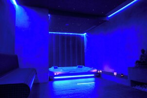 Un moderno spa con un jacuzzi iluminado en azul, una zona de estar y una estatua a la derecha.