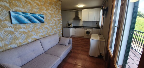 Un espace de vie compact comprenant un canapé, un lave-linge et un petit coin cuisine.