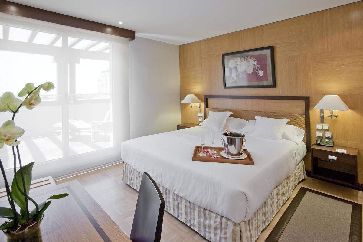 Una habitación de hotel con una cama grande, dos l ámparas de noche, un cuadro en la pared y una ventana con vistas.