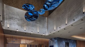 Ein moderner Empfangsbereich mit einem Marmor-Empfangstresen, Holzlamellen und einer blauen abstrakten Skulptur.
