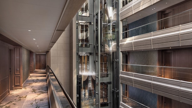 Ein moderner Hotelkorridor mit einem zentralen Aufzugsschacht, Holzvertäfelung an den Wänden und einem gemusterten Boden.