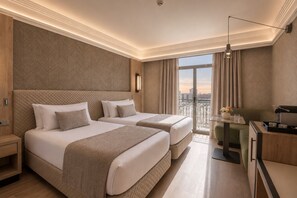 Une chambre d’hôtel avec deux lits, un bureau, une chaise, une machine à café et une vue sur la ville.