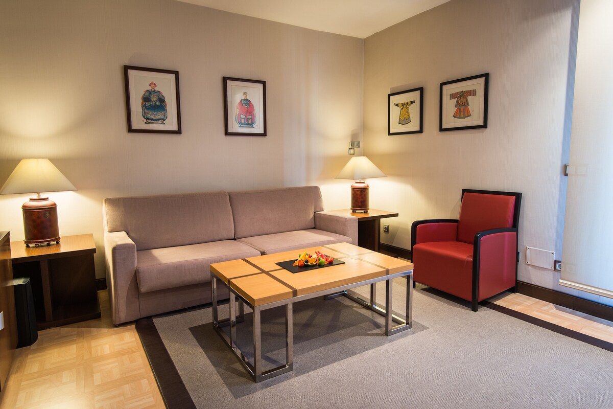 Un salon avec un canapé, un fauteuil rouge, une table basse et deux lampes.