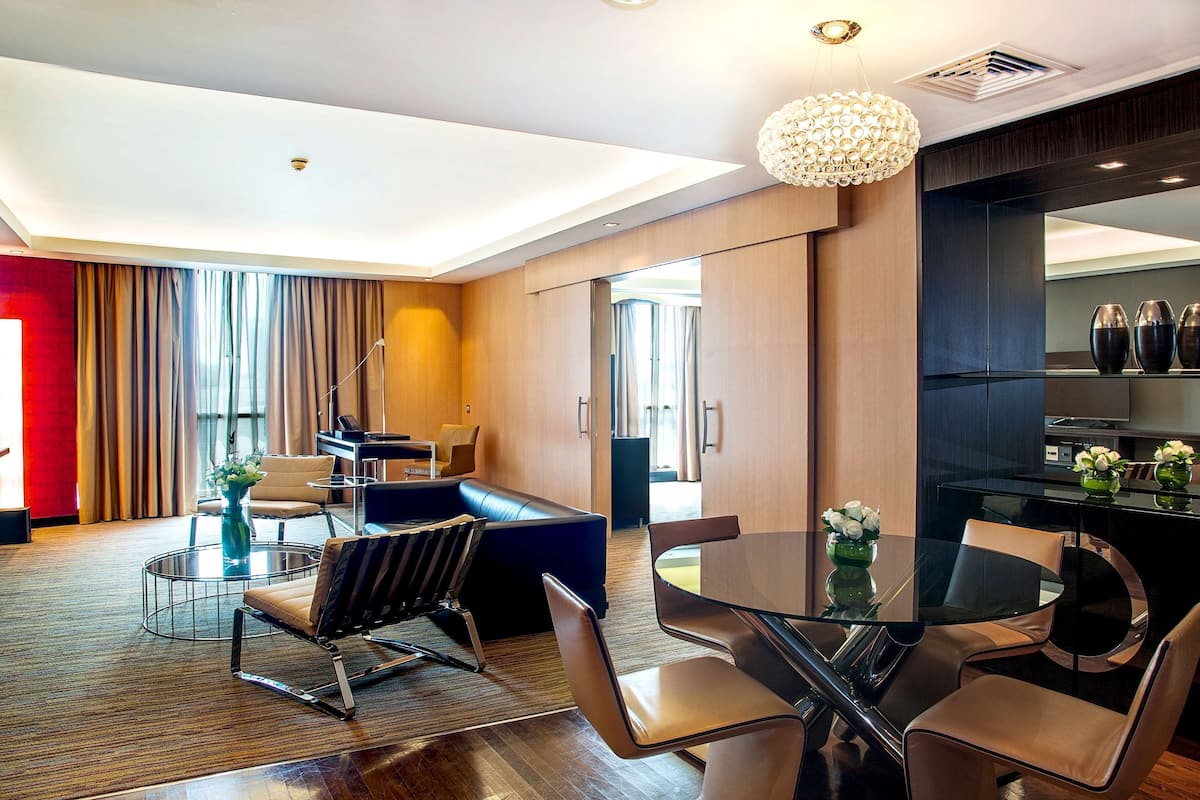 A modern hotel room with a dining area, a sofa, and a glass table.
