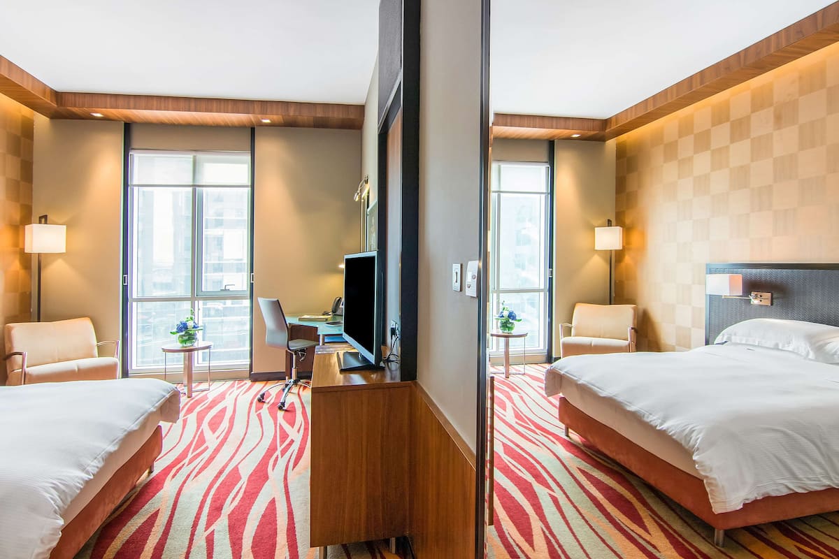 A hotel room with two beds, a desk with a TV, a chair, and a small table with a plant.