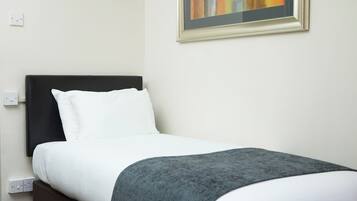 A neatly made bed with white linens and a gray throw blanket, a black headboard, and a framed abstract painting on the wall.