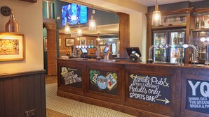 Una zona de bar con mostrador, pantallas digitales y una variedad de botellas.