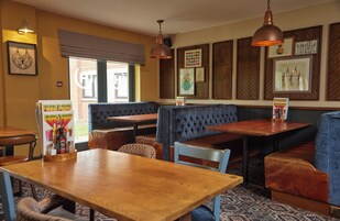 A restaurant interior with wooden tables, blue upholstered booths, and framed pictures on the walls.