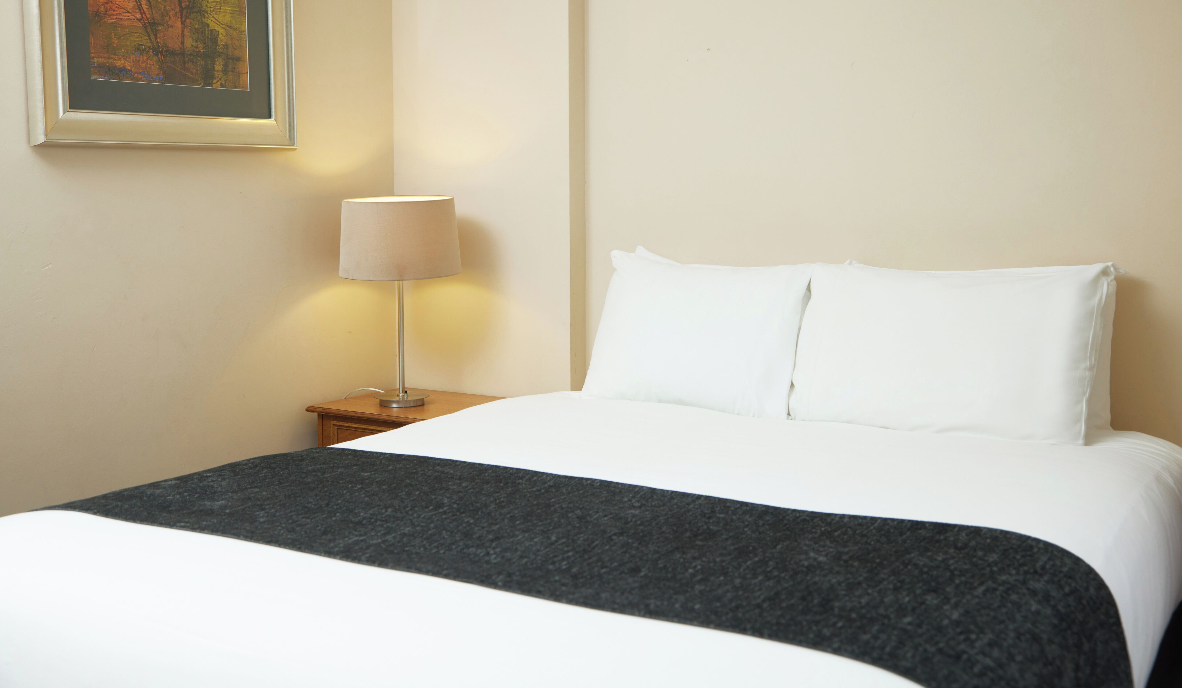 A neatly made bed with white linens and a dark gray throw blanket.