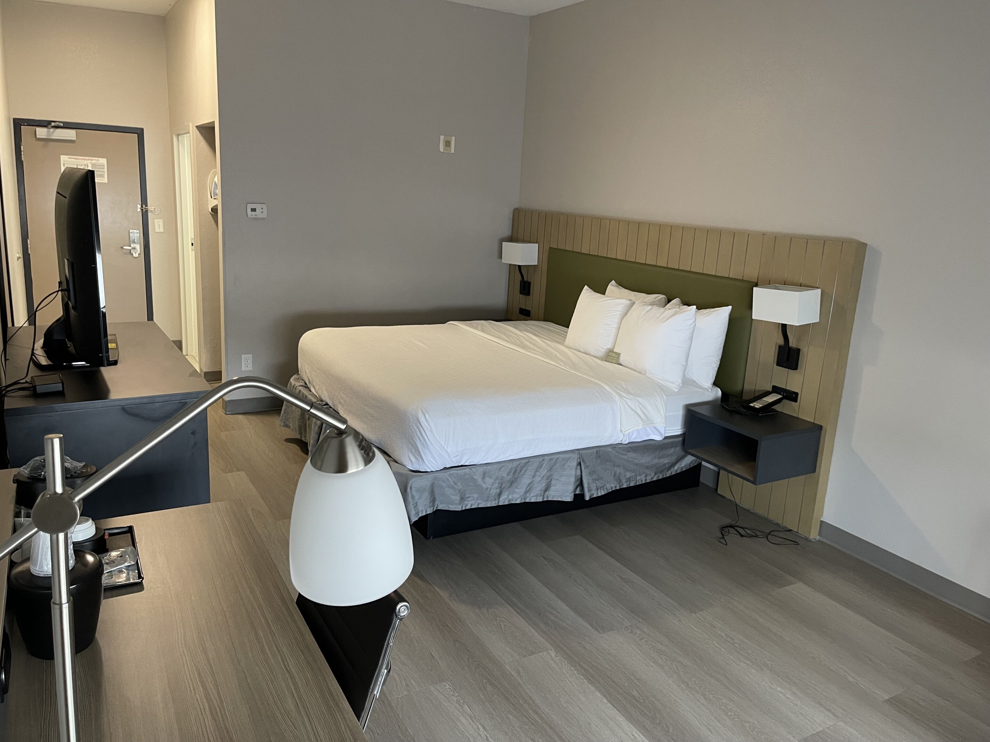 Quarto de hotel com cama, mesas de cabeceira, escrivaninha e abajur.
