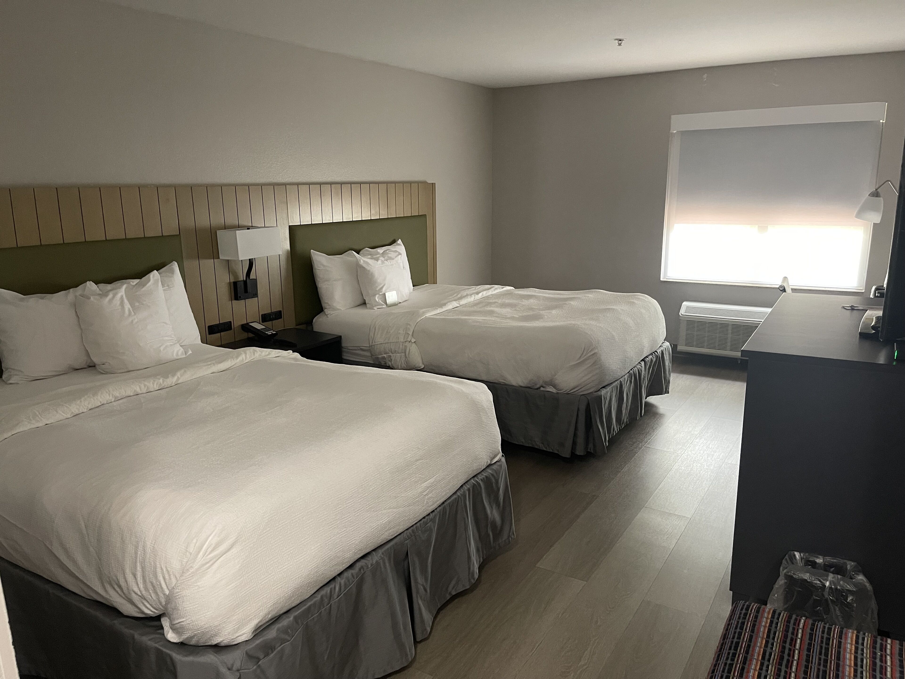 Habitació d'hotel amb dos llits, escriptori, cadira, làmpada i finestra.