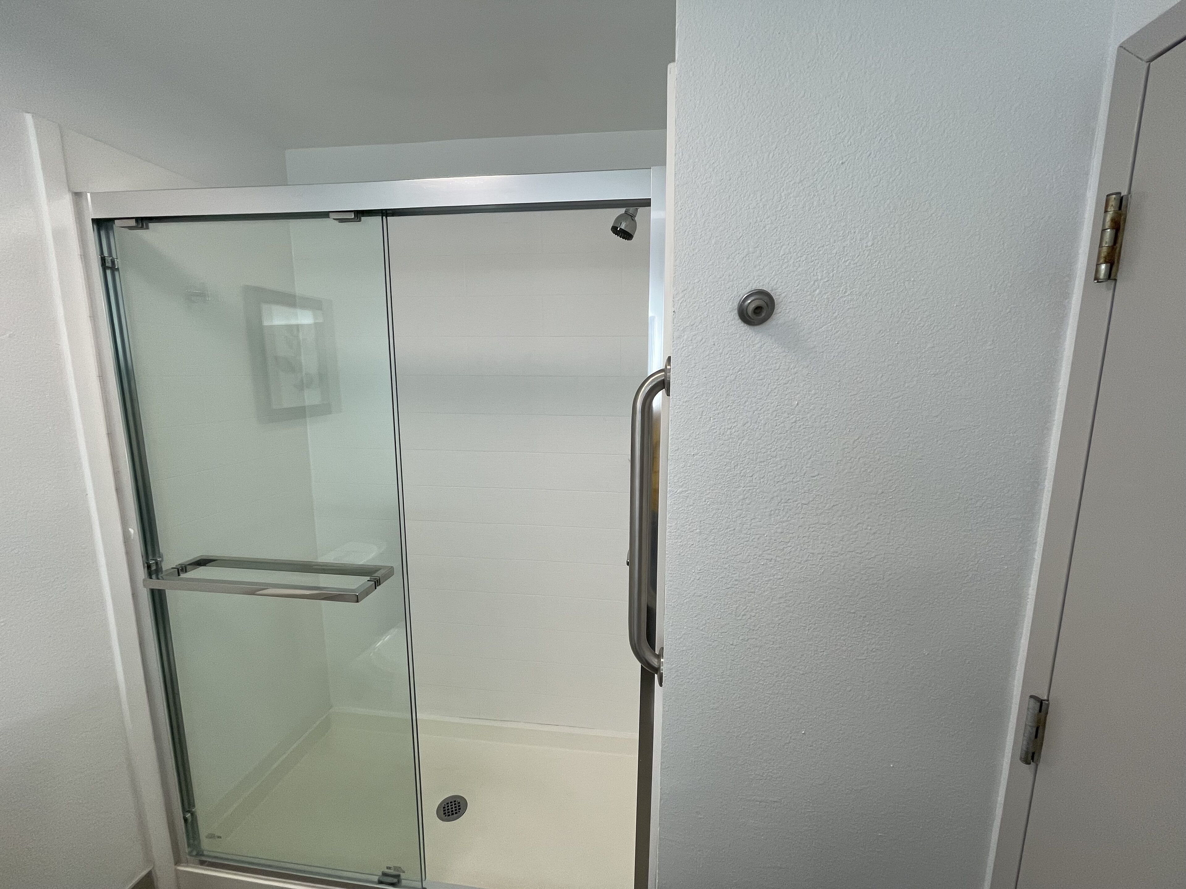 A glass-enclosed shower with a metal handle and a white tiled wall.