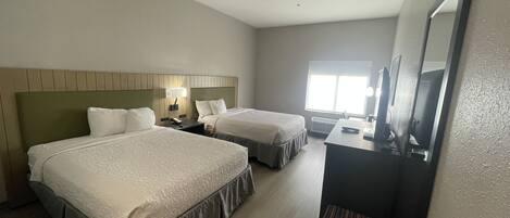 A hotel room with two beds, a desk, a chair, a mirror, and a window.