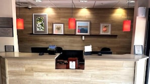 A reception desk with a wooden finish, a digital display, and framed artwork on the wall. - Country Inn & Suites by Radisson, Midway - Tallahassee West (Midway)