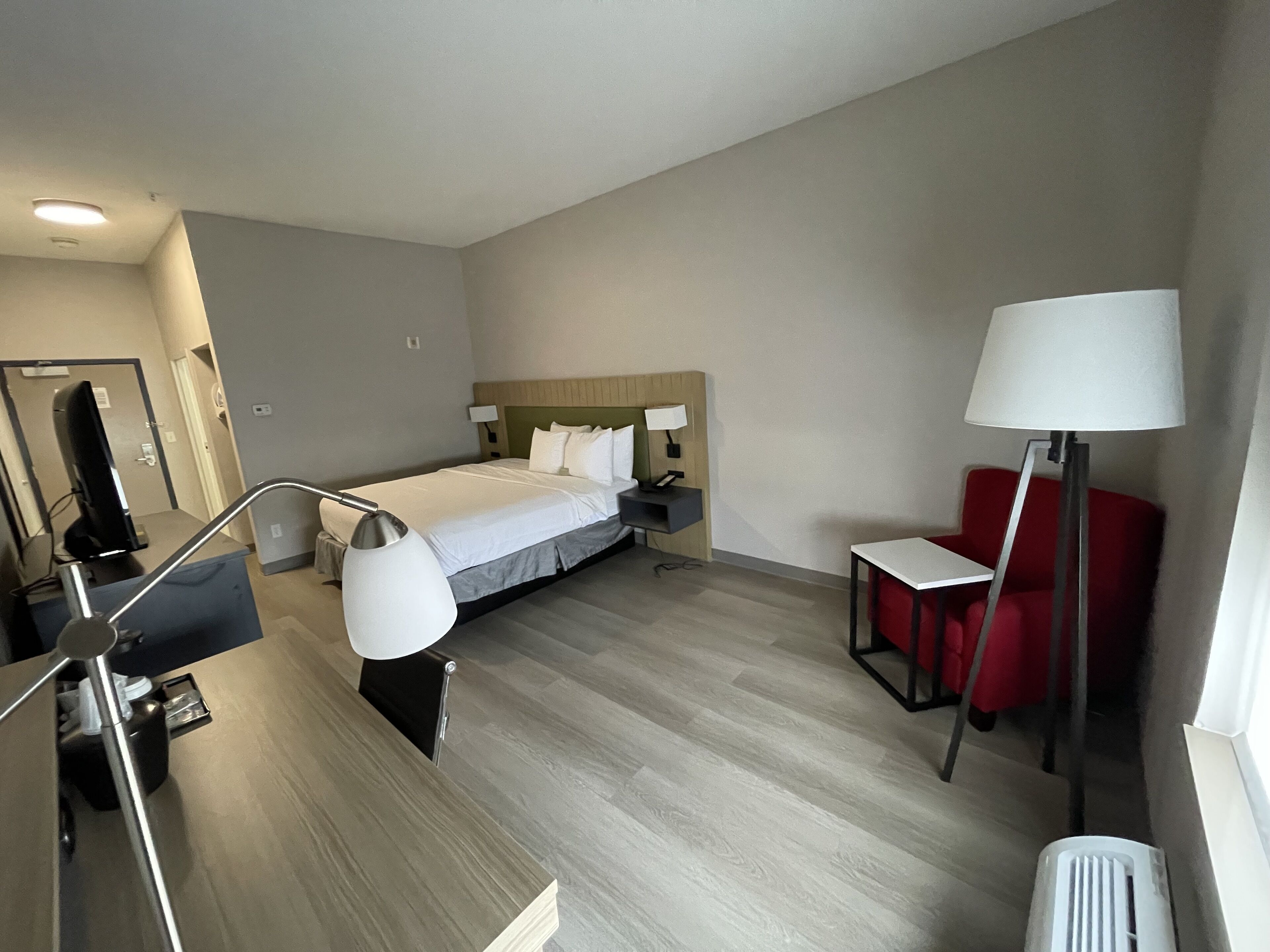A hotel room with a bed, bedside tables, a desk, a chair, and a lamp.
