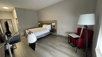 A hotel room with a bed, bedside tables, a desk, a chair, and a lamp.