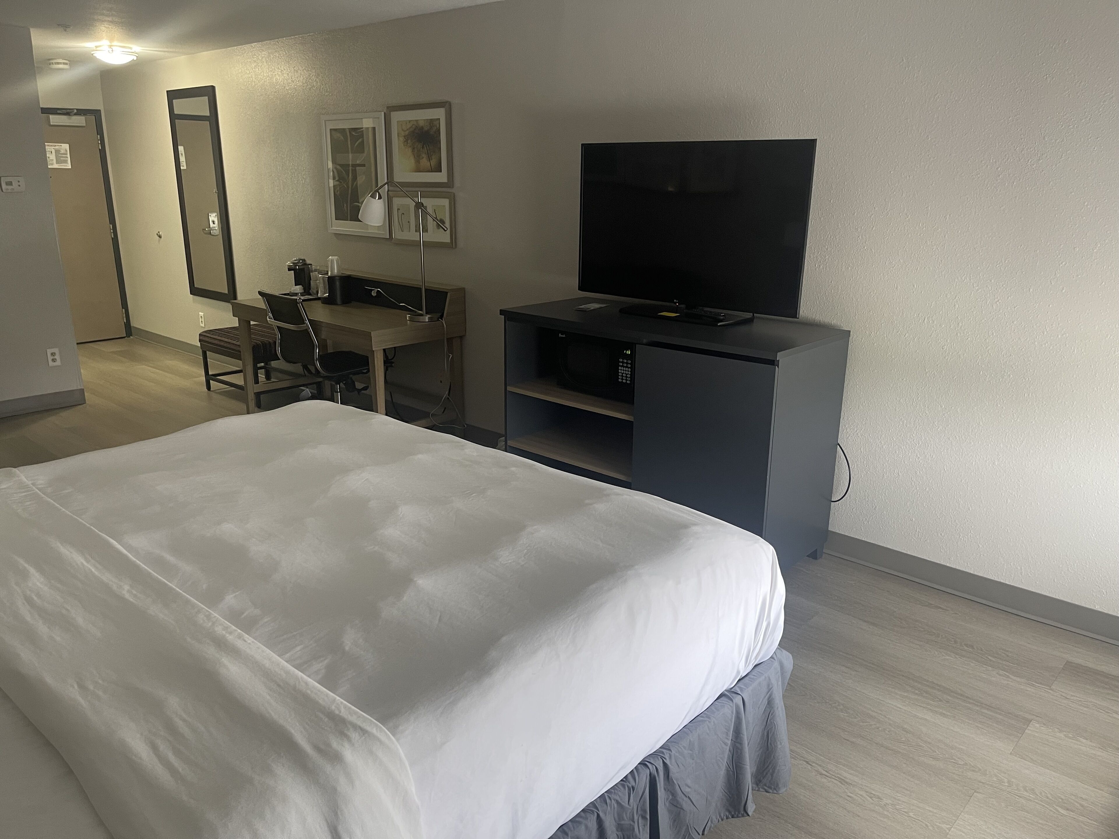 Ein Hotelzimmer mit einem großen Bett, einem Schreibtisch mit Computer, einem Flachbildfernseher und einer Mikrowelle.