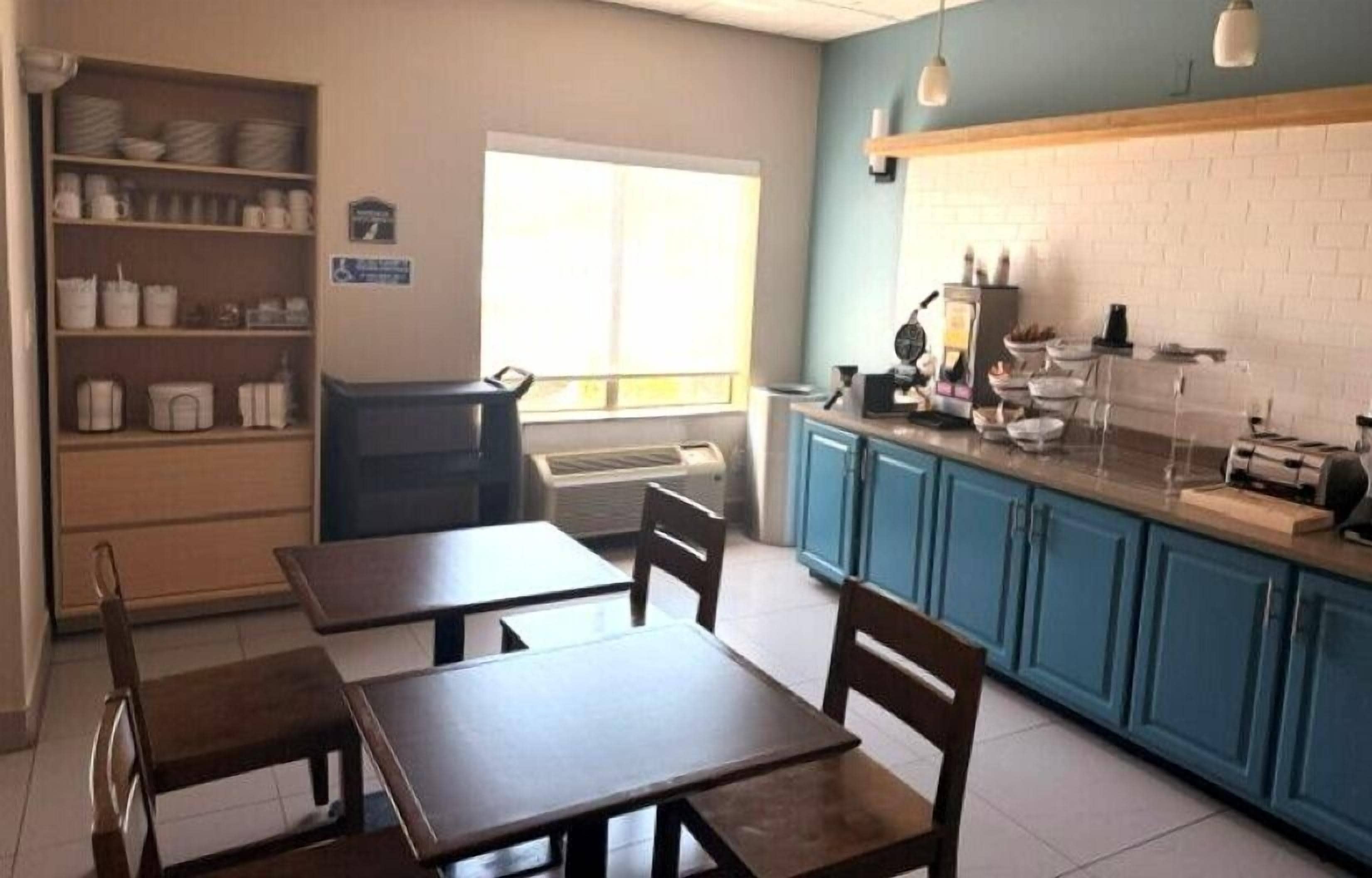 A dining area with tables and chairs, a kitchen counter with appliances, and a window providing natural light.