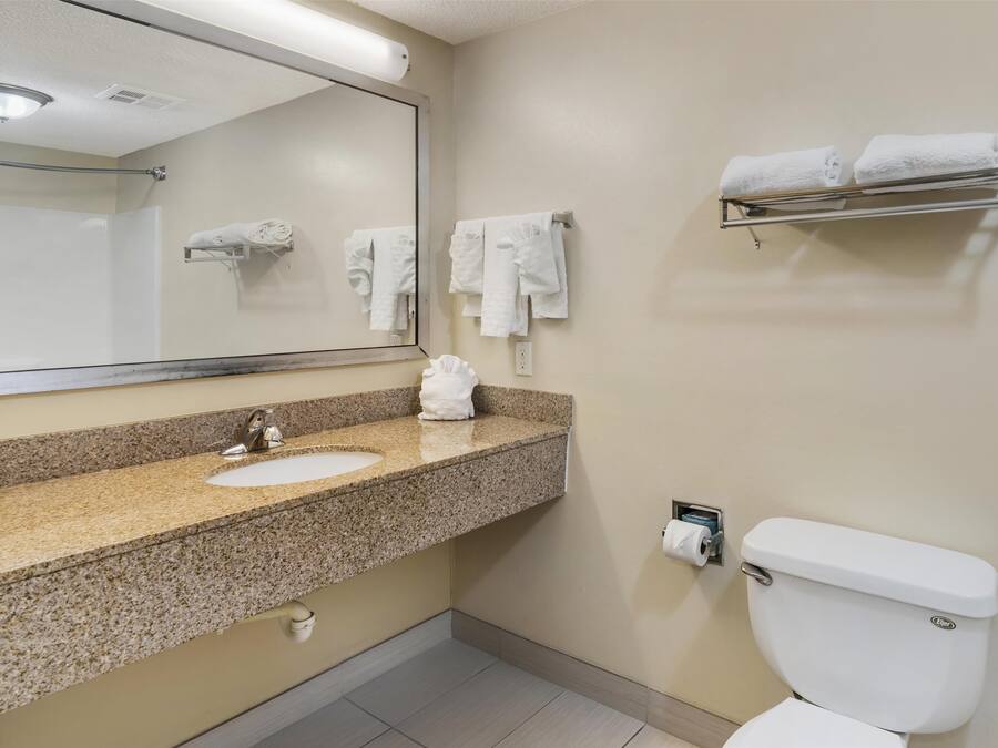 Een badkamer met een wastafel met granieten blad, een spiegel, een toilet en handdoekrekken.