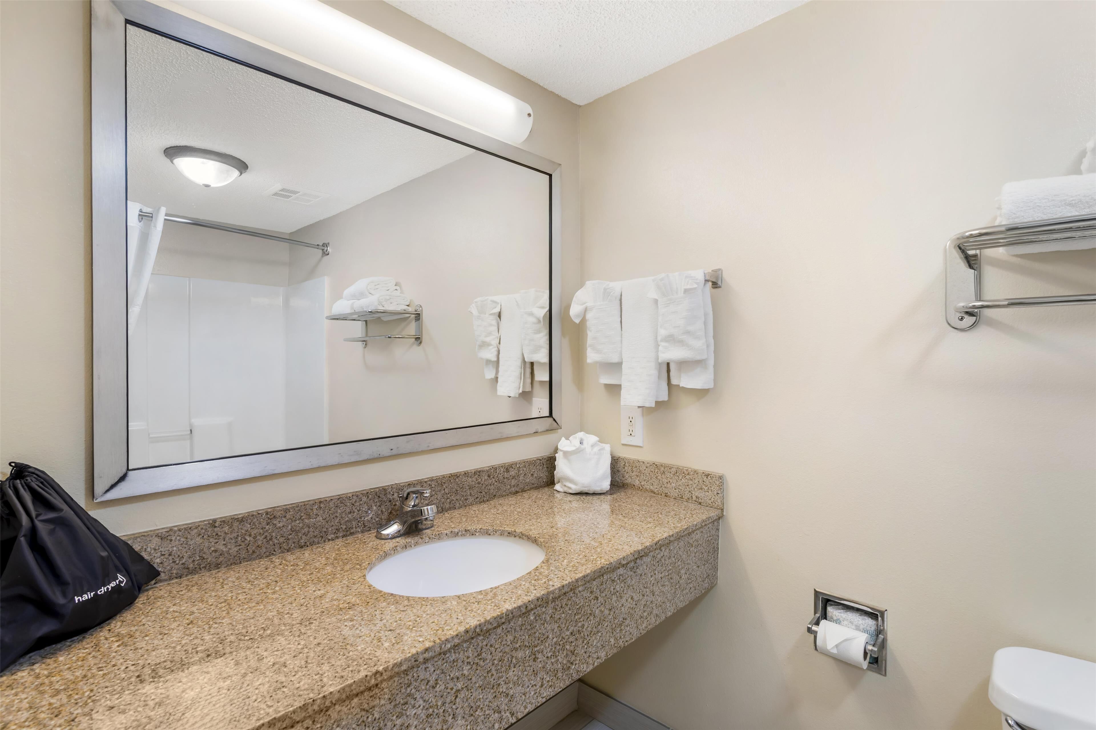 A bathroom with a large mirror, a sink, a towel rack, and a toilet.