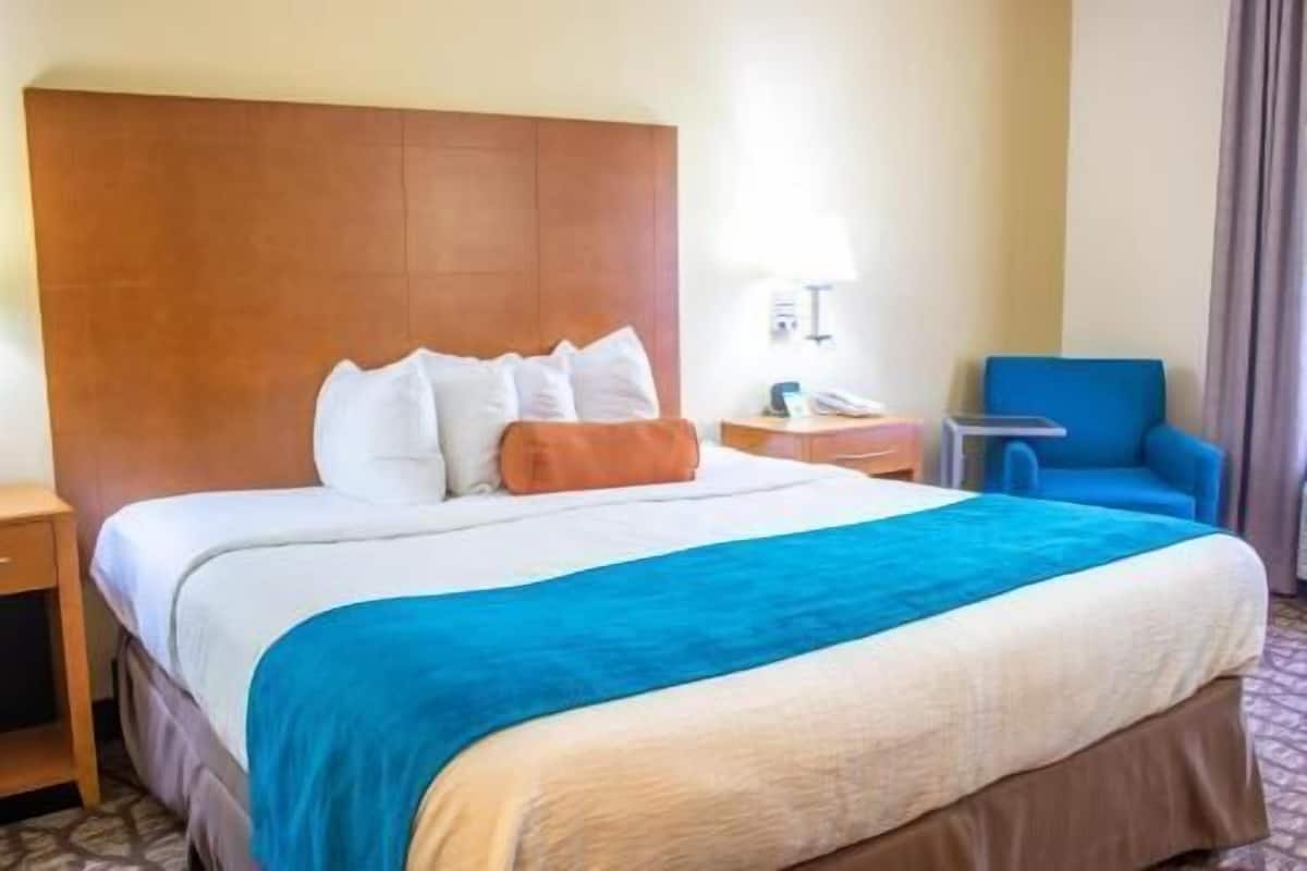 Una habitación de hotel con una cama grande, una mesita de noche, una silla y una lámpara.