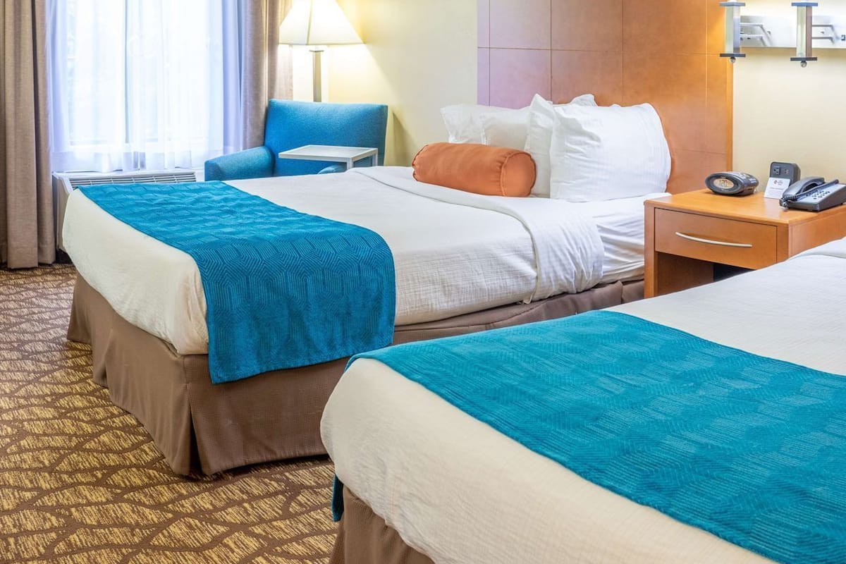 Habitación de hotel con dos camas, un escritorio, una silla, una lámpara y un teléfono.