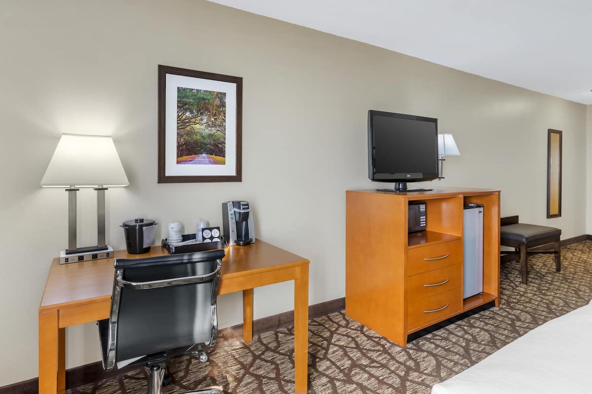 Una habitación de hotel con un escritorio de madera, una silla, un televisor sobre un mueble, una cafetera, un refrigerador y una cama.