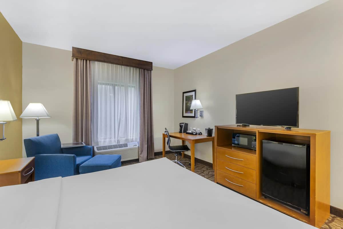 Una habitación de hotel con una cama, un escritorio con computadora, televisor y un mini bar.