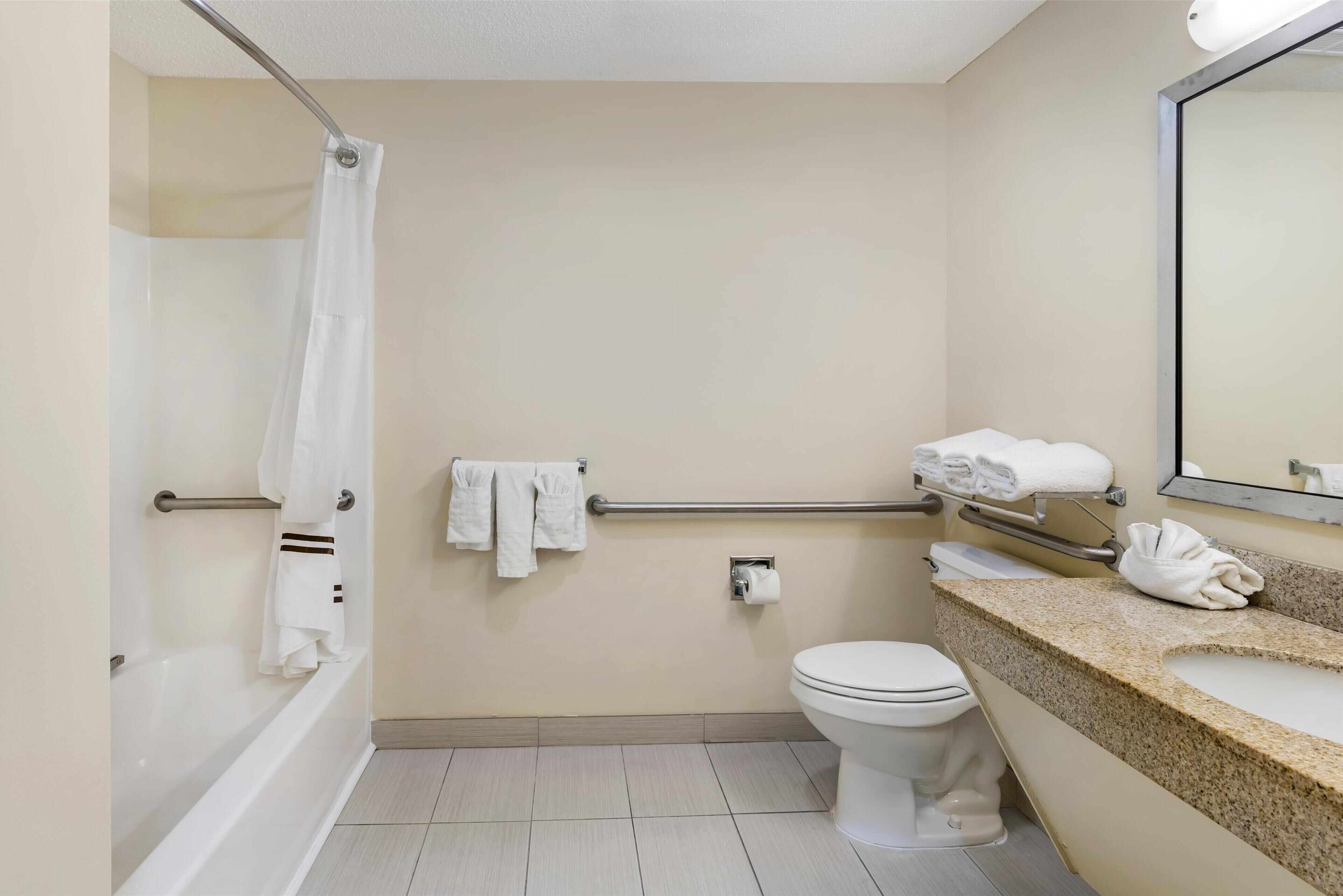 Un baño con bañera, inodoro y lavabo. Hay toallas colgadas en un perchero y un espejo sobre el lavabo.