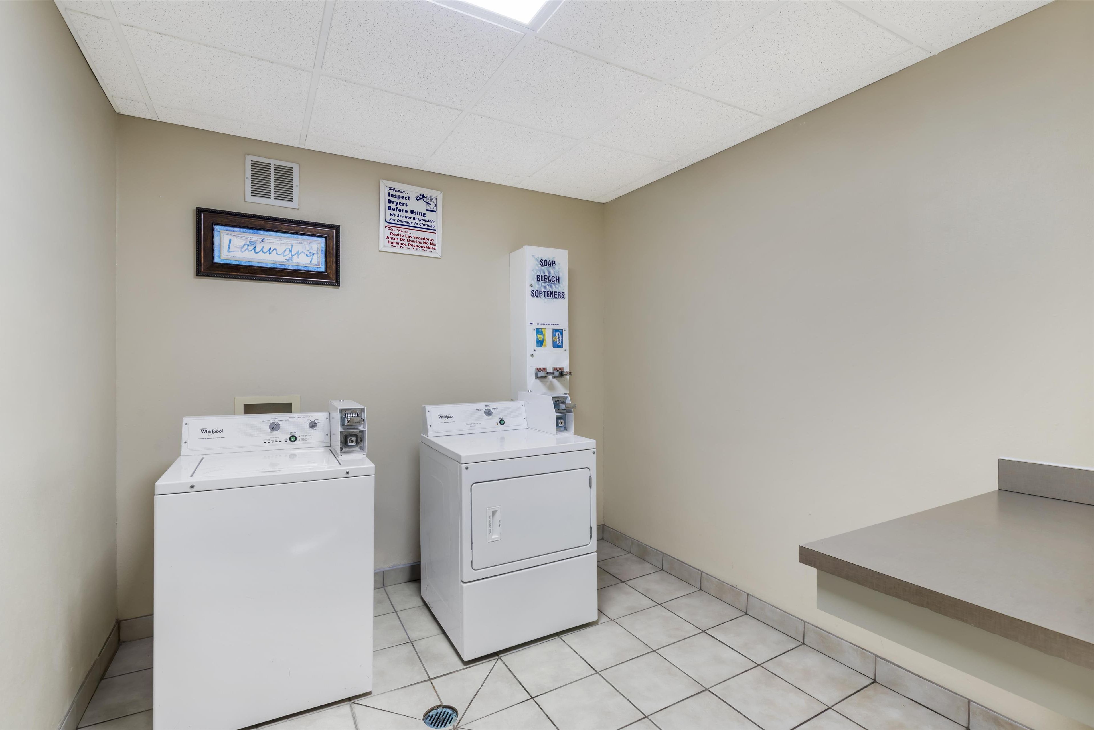 Uma lavanderia com duas máquinas de lavar e secar Whirlpool, um aviso para sabão, alvejante e amaciantes, e uma placa com a palavra "laundry".