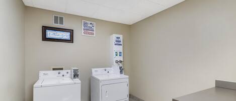 Uma lavanderia com duas máquinas de lavar e secar Whirlpool, um aviso para sabão, alvejante e amaciantes, e uma placa com a palavra "laundry".