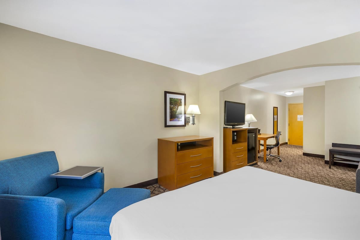 Habitación de hotel con cama, escritorio con silla, sofá azul, cómoda de madera y televisor.